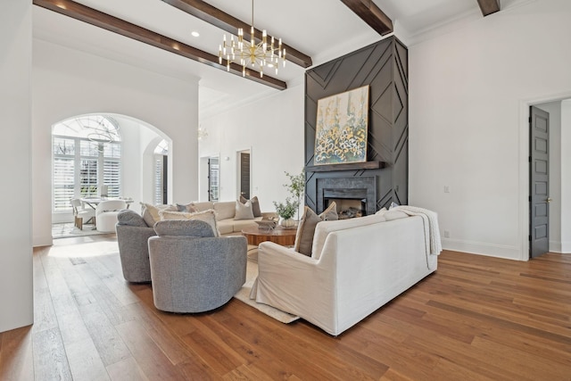 living room featuring wood finished floors, arched walkways, beam ceiling, a fireplace, and a notable chandelier