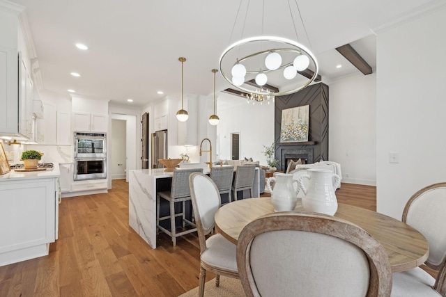 dining room featuring recessed lighting, beamed ceiling, a fireplace, light wood-style flooring, and a notable chandelier