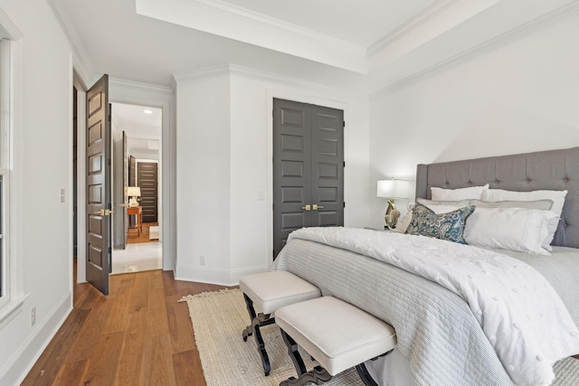 bedroom featuring baseboards, crown molding, wood finished floors, and a closet