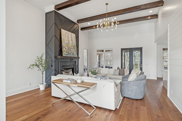 living area featuring hardwood / wood-style floors, an inviting chandelier, beamed ceiling, baseboards, and a fireplace