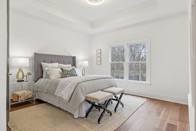bedroom with baseboards, crown molding, a tray ceiling, and light wood-type flooring