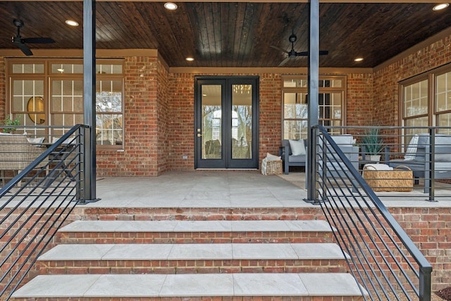 view of exterior entry with ceiling fan, french doors, and brick siding