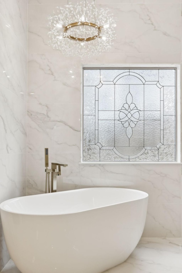 bathroom featuring tile walls, marble finish floor, a notable chandelier, and a freestanding bath