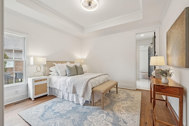 bedroom with crown molding, wood finished floors, a raised ceiling, baseboards, and visible vents