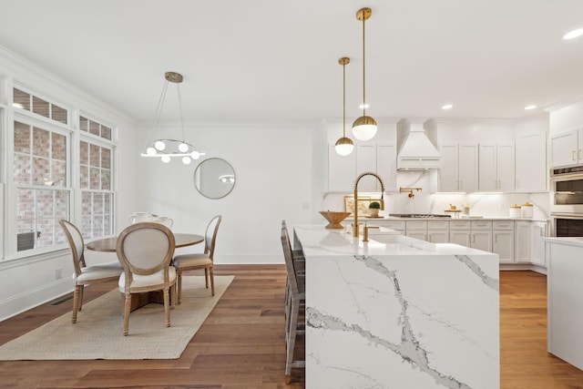 kitchen featuring wood finished floors, stainless steel appliances, premium range hood, baseboards, and light stone countertops