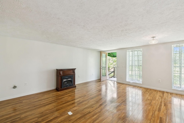 unfurnished living room featuring a glass covered fireplace, baseboards, wood finished floors, and a textured ceiling