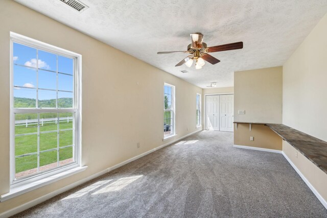 carpeted spare room with ceiling fan, baseboards, a textured ceiling, and visible vents