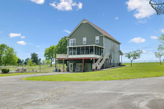 back of house featuring stairway, aphalt driveway, fence, a yard, and a sunroom