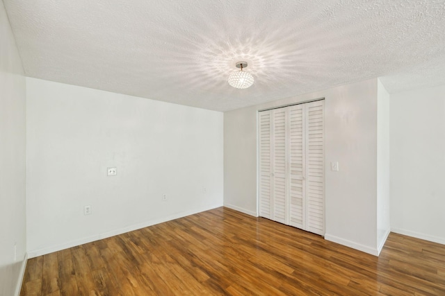 unfurnished bedroom with a closet, wood finished floors, a textured ceiling, and baseboards
