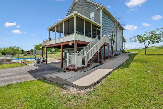 rear view of property with stairway, a fenced in pool, a patio, a lawn, and a sunroom