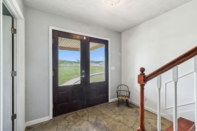 entrance foyer featuring french doors, a textured ceiling, baseboards, concrete flooring, and stairs