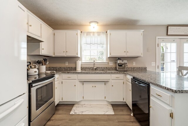kitchen with a sink, freestanding refrigerator, a peninsula, black dishwasher, and stainless steel range with electric stovetop