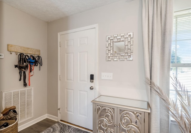 foyer with dark wood finished floors, baseboards, a textured ceiling, and visible vents