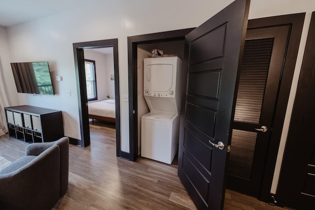 laundry area with stacked washer and clothes dryer, wood finished floors, baseboards, and laundry area