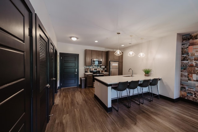 kitchen with a sink, a kitchen bar, a peninsula, appliances with stainless steel finishes, and dark wood-style floors