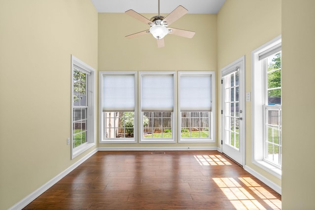 unfurnished sunroom with a high ceiling, wood finished floors, visible vents, and baseboards