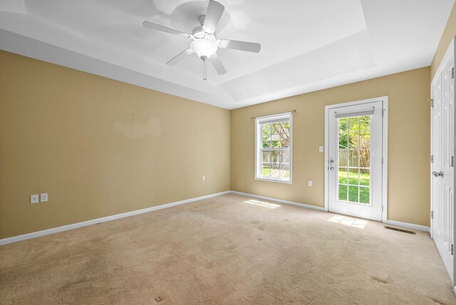 empty room featuring a tray ceiling, visible vents, a ceiling fan, baseboards, and light colored carpet