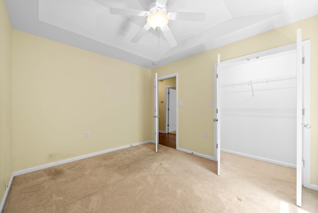 unfurnished bedroom featuring a closet, ceiling fan, light carpet, a tray ceiling, and baseboards