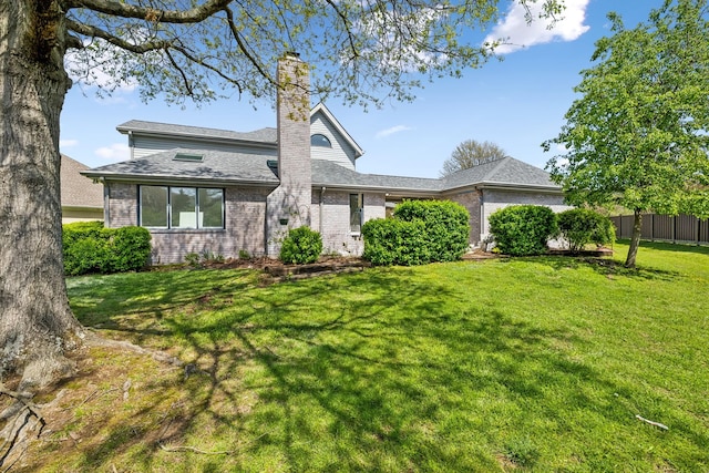 rear view of property with a chimney, brick siding, fence, and a yard