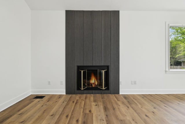 interior details with baseboards, visible vents, wood finished floors, and a glass covered fireplace