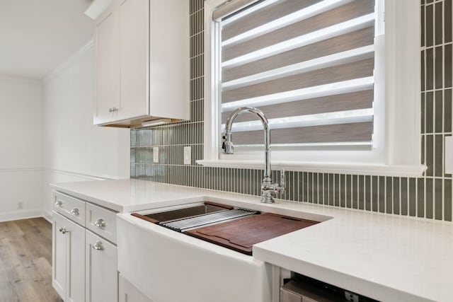 kitchen with a sink, decorative backsplash, white cabinetry, light countertops, and ornamental molding