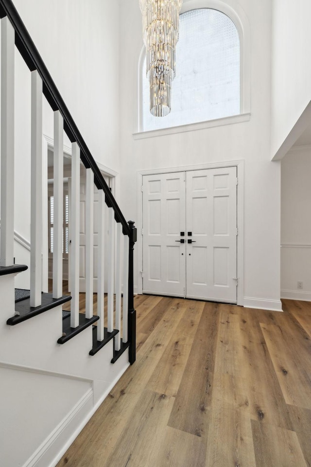 foyer with stairs, an inviting chandelier, a high ceiling, and wood finished floors