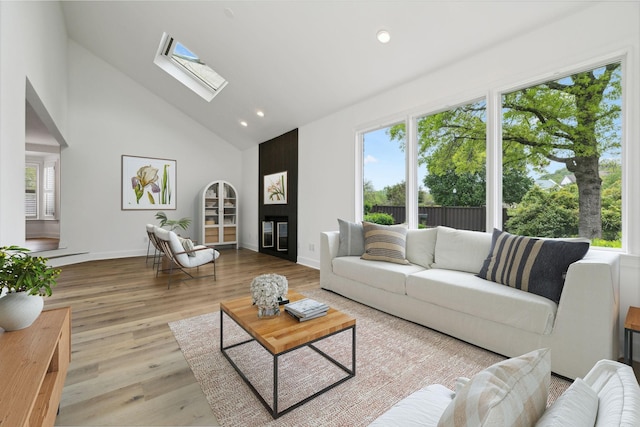 living room with recessed lighting, high vaulted ceiling, baseboards, a skylight, and wood finished floors