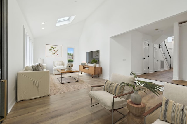 living area featuring a skylight, wood finished floors, stairs, baseboards, and high vaulted ceiling