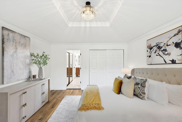 bedroom featuring a raised ceiling, a closet, an inviting chandelier, ornamental molding, and wood finished floors