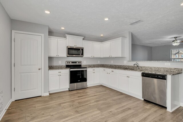 kitchen with stainless steel appliances, a sink, a peninsula, light wood-style flooring, and ceiling fan