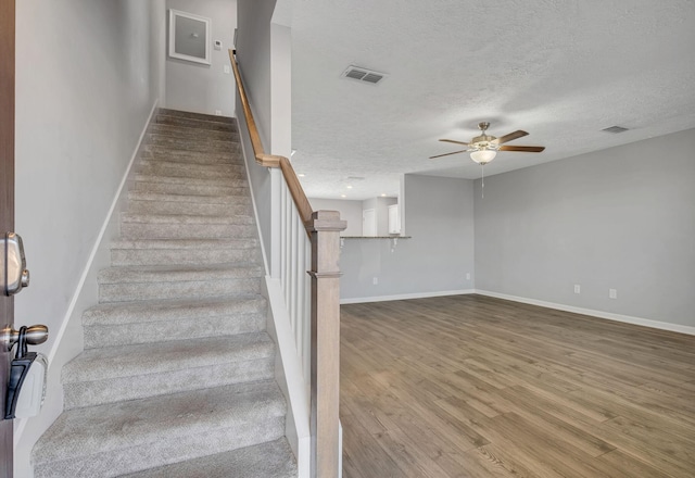 stairway with a textured ceiling, baseboards, visible vents, a ceiling fan, and wood finished floors