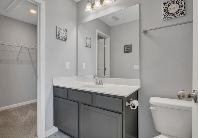 bathroom with toilet, visible vents, baseboards, vanity, and a walk in closet