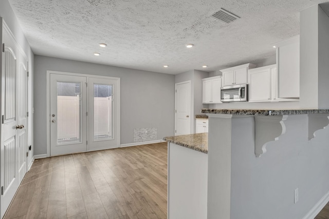 kitchen with a kitchen bar, stainless steel microwave, baseboards, and white cabinets