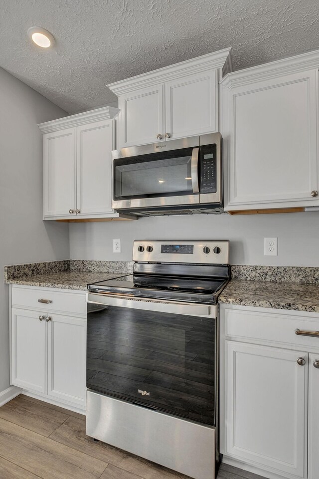 kitchen with light stone counters, a textured ceiling, light wood-style flooring, white cabinets, and appliances with stainless steel finishes