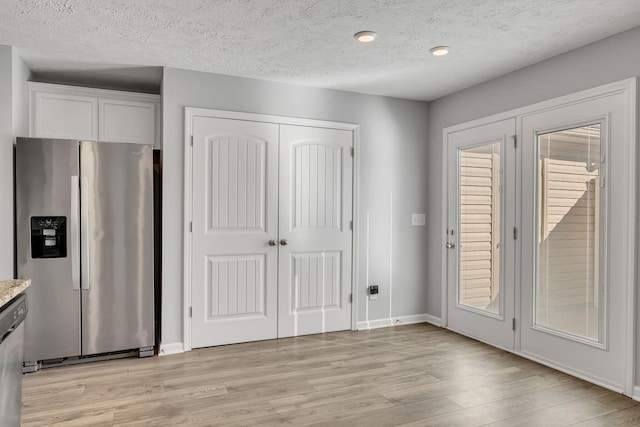 interior space featuring light wood-style flooring, baseboards, and a textured ceiling