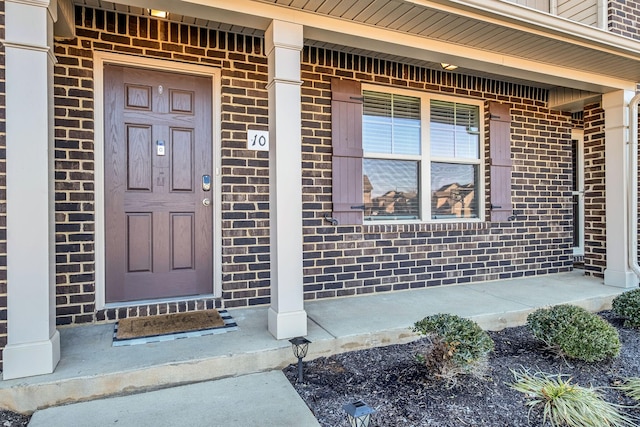 view of exterior entry featuring covered porch and brick siding