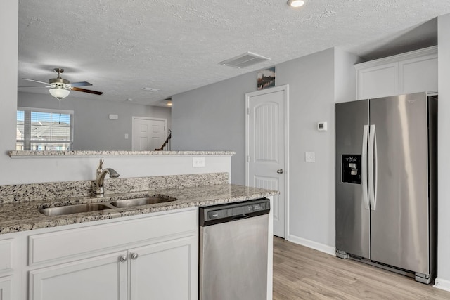 kitchen featuring stainless steel appliances, light wood-style flooring, a sink, a textured ceiling, and visible vents