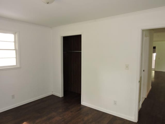 unfurnished bedroom with baseboards, a closet, ornamental molding, and dark wood finished floors