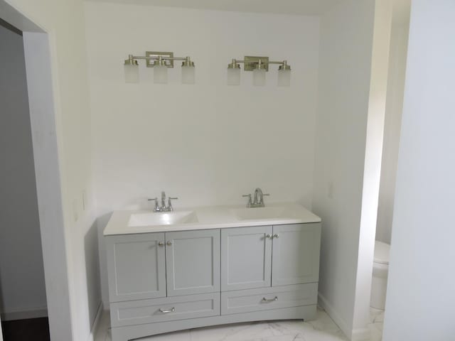 bathroom with marble finish floor, toilet, a sink, and double vanity