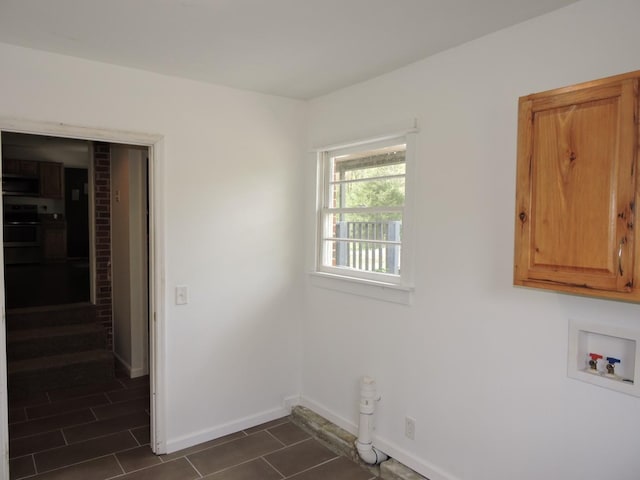 washroom featuring baseboards, cabinet space, dark tile patterned flooring, and washer hookup