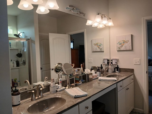 bathroom featuring an inviting chandelier, a shower with door, a sink, and double vanity