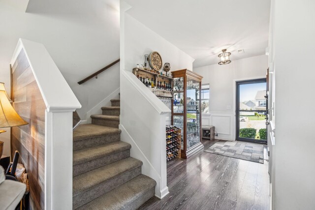 entrance foyer with wood finished floors, a decorative wall, stairs, and wainscoting