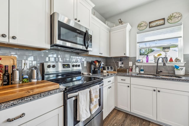 kitchen with dark stone countertops, a sink, decorative backsplash, appliances with stainless steel finishes, and white cabinetry