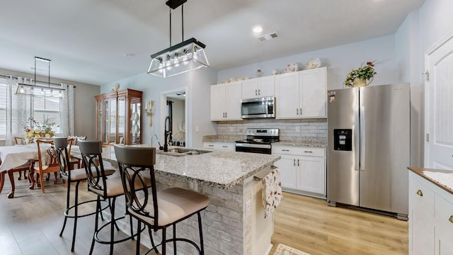 kitchen with stainless steel appliances, a sink, white cabinetry, hanging light fixtures, and backsplash