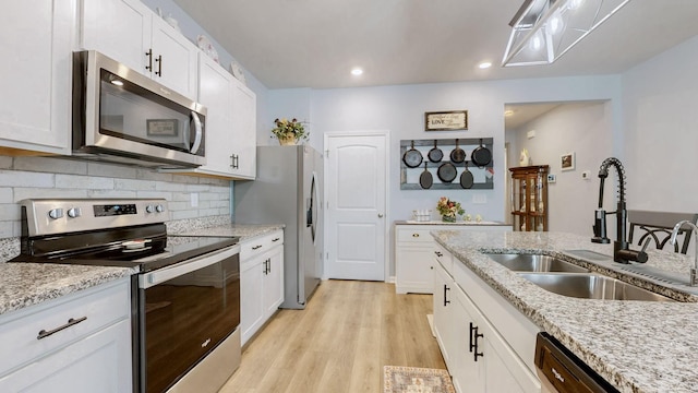 kitchen featuring stainless steel appliances, a sink, light wood finished floors, decorative backsplash, and white cabinetry