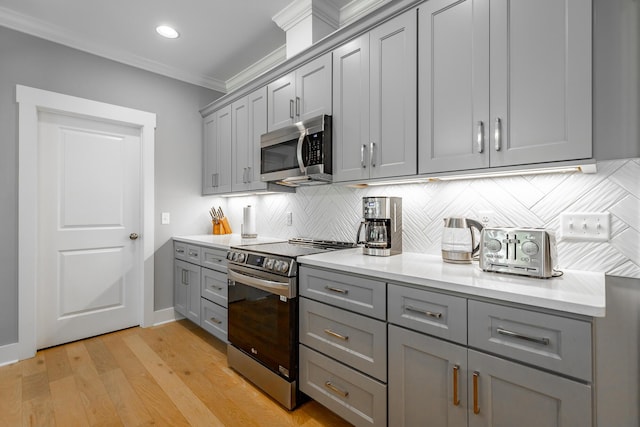 kitchen with light wood-type flooring, decorative backsplash, gray cabinetry, light countertops, and appliances with stainless steel finishes