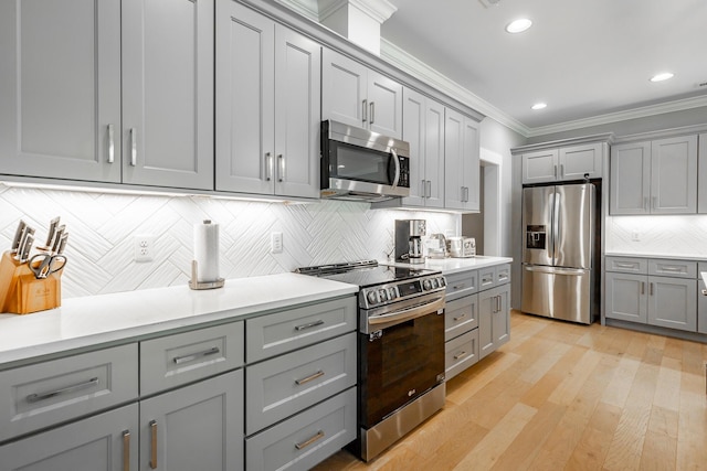 kitchen with crown molding, stainless steel appliances, light countertops, backsplash, and gray cabinetry