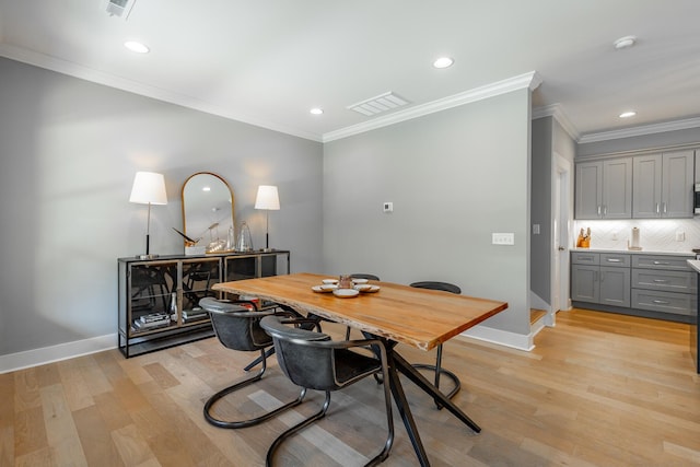dining room with light wood-style flooring, visible vents, crown molding, and baseboards