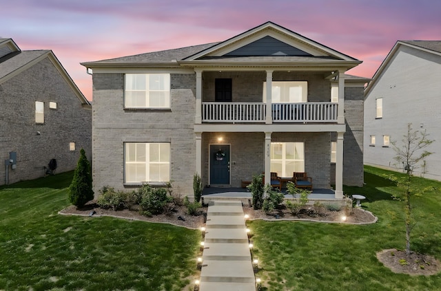 view of front of home featuring a front lawn, brick siding, a balcony, and covered porch