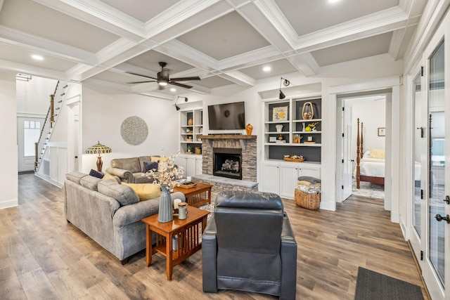 living room featuring coffered ceiling, wood finished floors, a stone fireplace, a ceiling fan, and beamed ceiling
